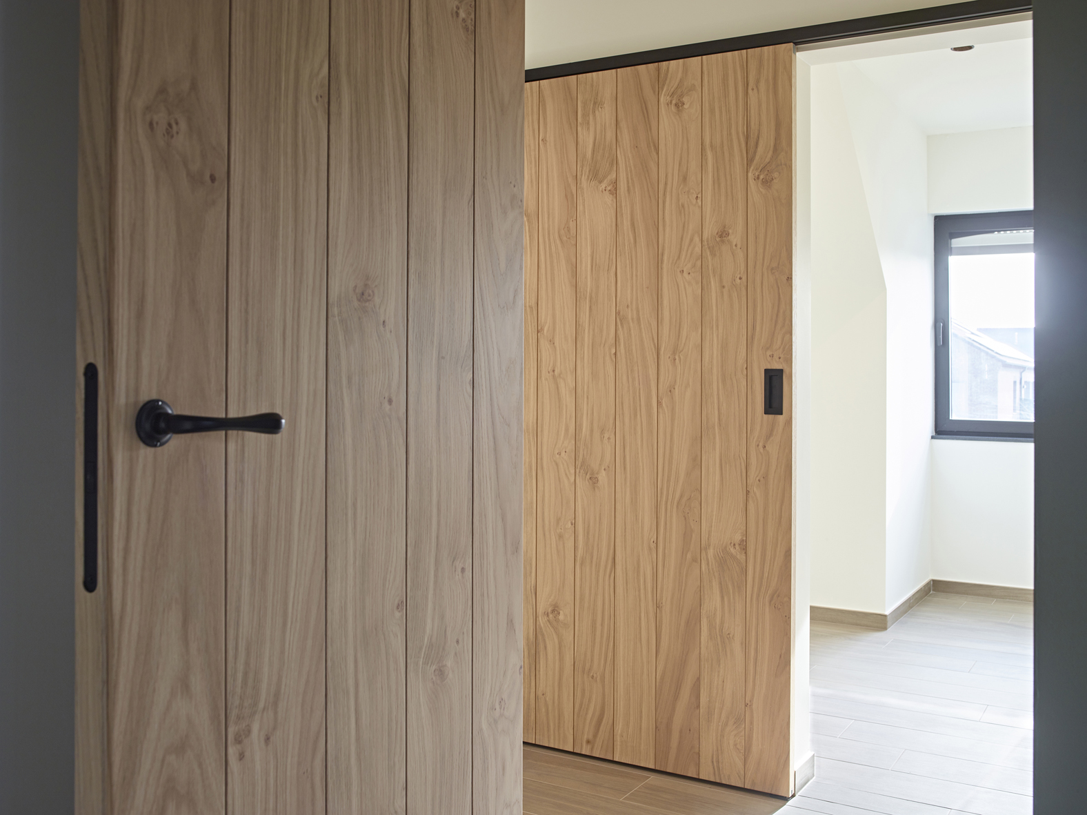 Houten schuifdeur bevestigd met zwarte aluminium muurbevestiging van ARLU (Argenta). 