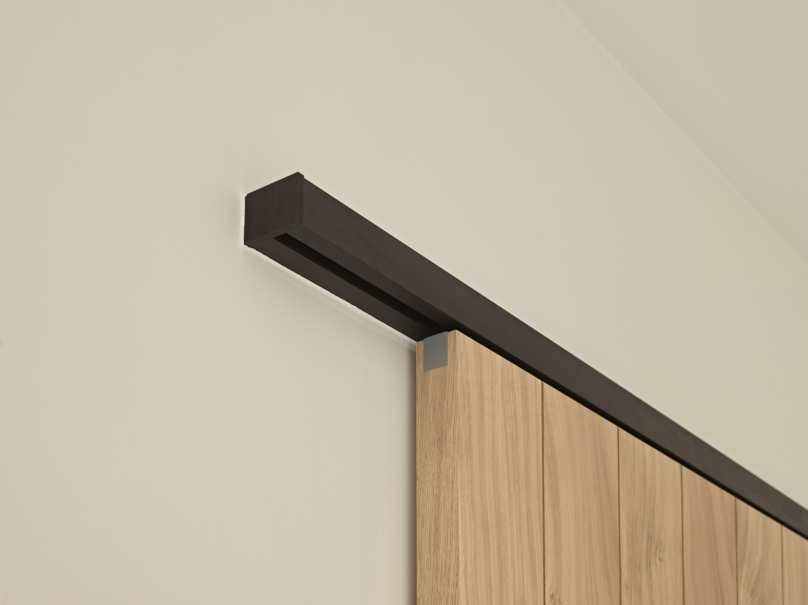 Houten schuifdeur bevestigd met zwarte aluminium muurbevestiging van ARLU (Argenta). 