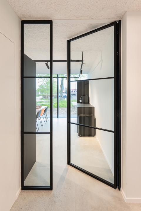 Zwarte glazen scheidingswand gecombineerd met glazen draaideur (product: divina ARLU) geïnstalleerd bij MFI Coatings.